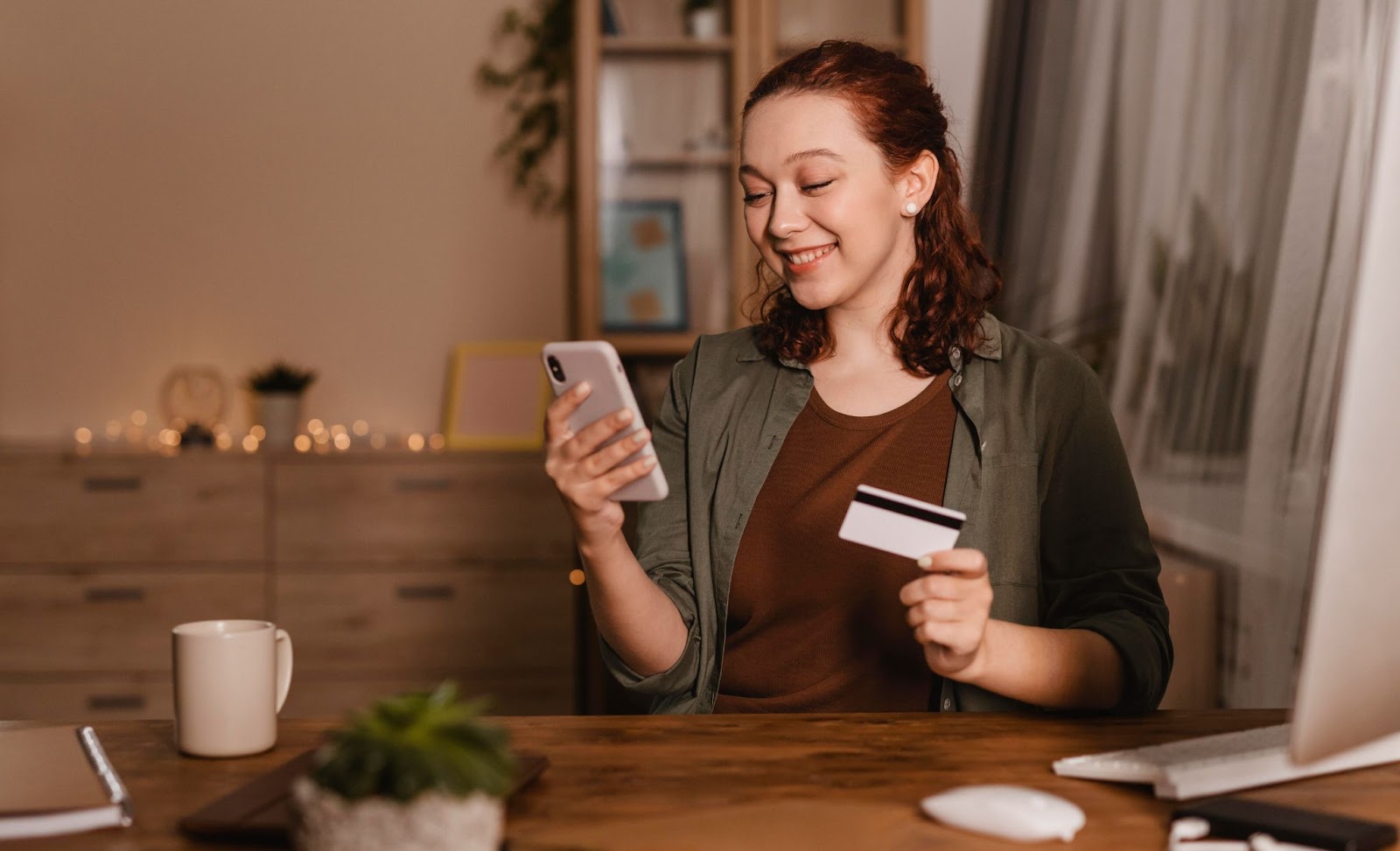 Una mujer sonriente sosteniendo un teléfono y una tarjeta de crédito